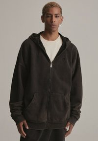 Czarna hoodie na zamek, wykonana z miękkiego materiału, z przednią kieszenią, ściągaczami przy rękawach oraz kapturem. Design ma zużytą teksturę i minimalistyczne logo.