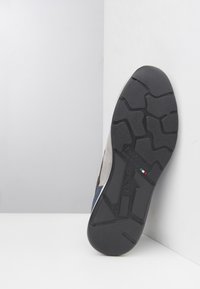 La suola della scarpa presenta un gomma nera texturizzata con un motivo a battistrada, completata da una parte superiore grigia, che mostra un design elegante e un marchio italiano.