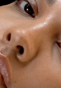 Primer plano de un tono de piel, destacando una textura suave, una nariz prominente con fosas nasales visibles y un ojo oscuro y reflectante.