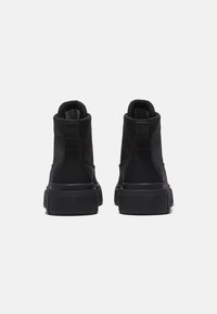 Zapatillas altas negras con parte superior texturizada, talón reforzado y suela de goma negra gruesa. Presentan un detalle de correa trasera ajustable.