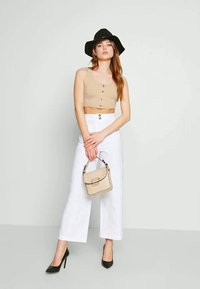 Top cropped bege com botões, calças brancas de cintura alta e perna larga, sapatos de salto agudo pretos e uma mala texturizada em bege claro.