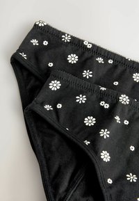 Zwarte katoenonderbroek met een witte bloemenprint, voorzien van een zachte textuur en een elastische tailleband. Afgewerkt met net stikwerk.