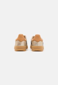 Baskets basses beiges et marron clair avec semelles en gomme vues de dos, dotées d'un rembourrage au talon et du logo GANT sur la semelle.