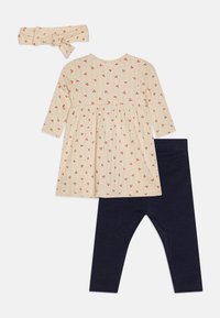 Cremefarbenes Kleid mit Blumenmuster, Falten, langen Ärmeln und Rundhalsausschnitt, kombiniert mit dunkelblauen Leggings und einem passenden Stirnband.