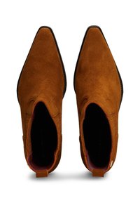 Bottines à bout pointu en daim marron clair avec une texture lisse. Présentent un doublage bordeaux contrastant et des accents de couture minimaux.