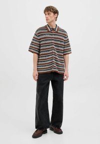 Chemise à manches courtes avec des rayures marron, noire et blanche, de coupe décontractée. Porte avec un jean noir à jambes larges et des chaussures marron.