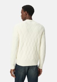 Cremfarbener Strickpullover mit einem Rautenmuster und gerippten Bündchen und Saum, kombiniert mit dunklen Jeans.
