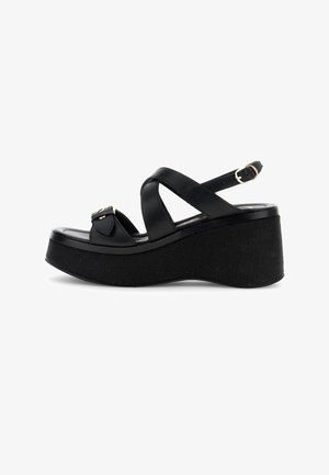 Sandalia de cuña plataforma negra con amplias correas cruzadas, hebilla en el tobillo y suela gruesa texturizada.