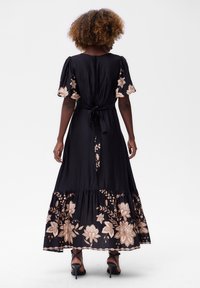 Zwarte maxi-jurk met korte pofmouwen, voorzien van rosegouden bloemenbroderie aan de onderste zoom en een strik in de taille.