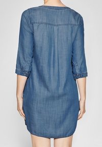 Denim-mekko, jossa on pyöreä pääntie, kolme neljännestä hihasta ja suora leikkaus, jossa on hieman kaareva helma. Vaaleansininen väri, pehmeä rakenne.
