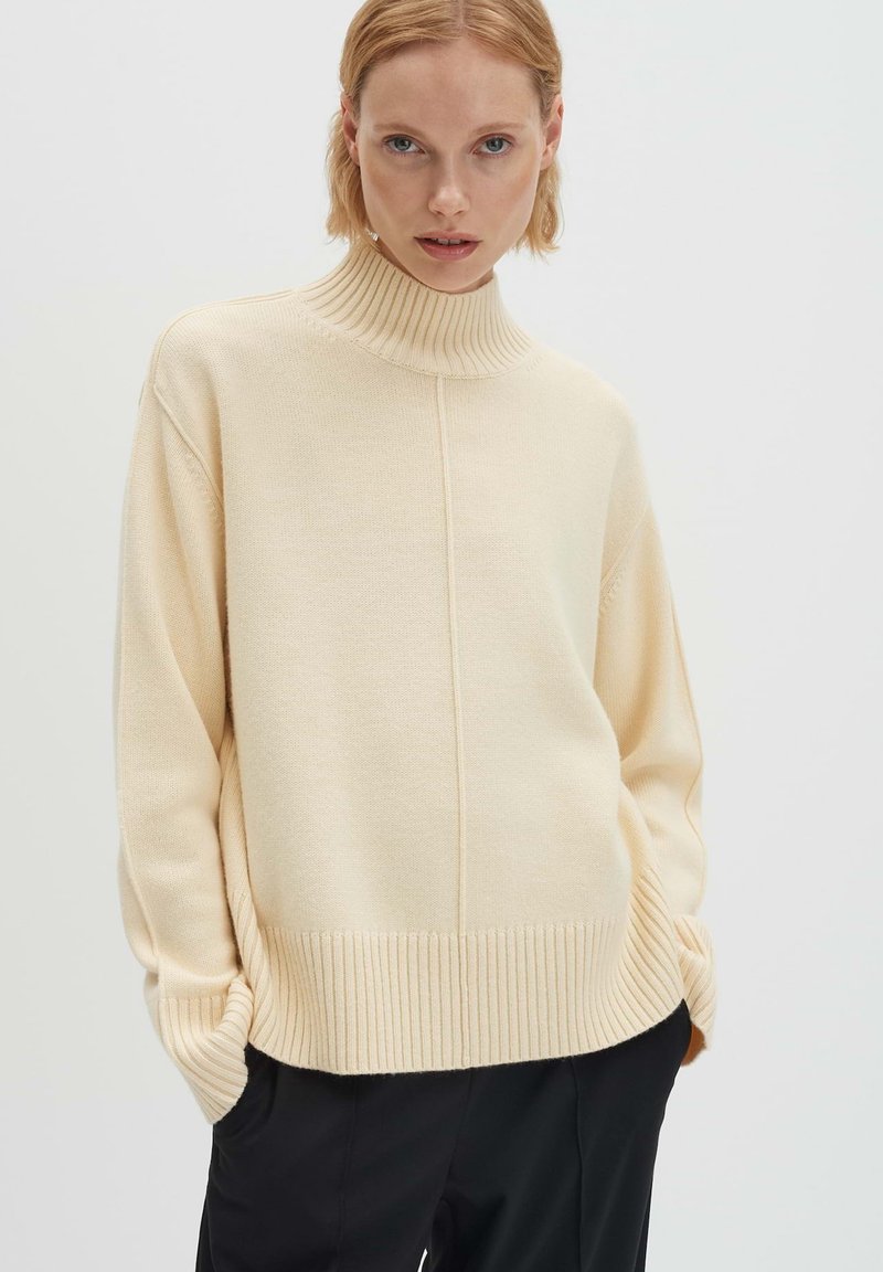 Cremefarbener Rollkragenpullover aus weichem Strickmaterial, mit geripptem Saum und Bündchen, legerer Passform und zentraler vertikaler Naht.