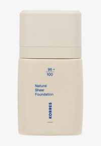 Bouteille rectangulaire beige avec un bouchon cylindrique, étiquetée "Fond de teint naturel transparent", avec du texte bleu. Surface lisse, design minimal.