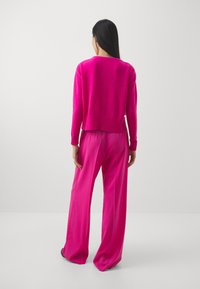 Fuksia neulepusero, jossa on lyhyt malli ja raidoitettu helma, yhdistettynä leveälahkeisiin fuksianvärisiin housuihin. Kangas näyttää pehmeältä ja suoralta.