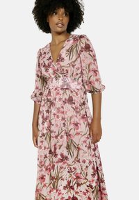 Floral maxi-jurk in lichtroze, met een diepe V-hals, driekwartmouwen en een getailleerde taille. De stof heeft een soepele textuur met een floral patroon.