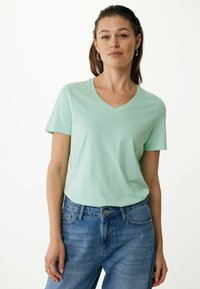 Mátově zelené tričko s výstřihem do V vyrobené z měkké látky, krátké rukávy, ve spojení se světle modrými džíny s vysokým pasem. Jednoduchý design, žádné viditelné vzory.