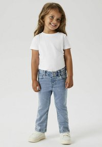 T-shirt blanc à manches courtes associé à un jean en denim bleu clair et des baskets blanches. Le jean a une coupe classique avec des poches avant.