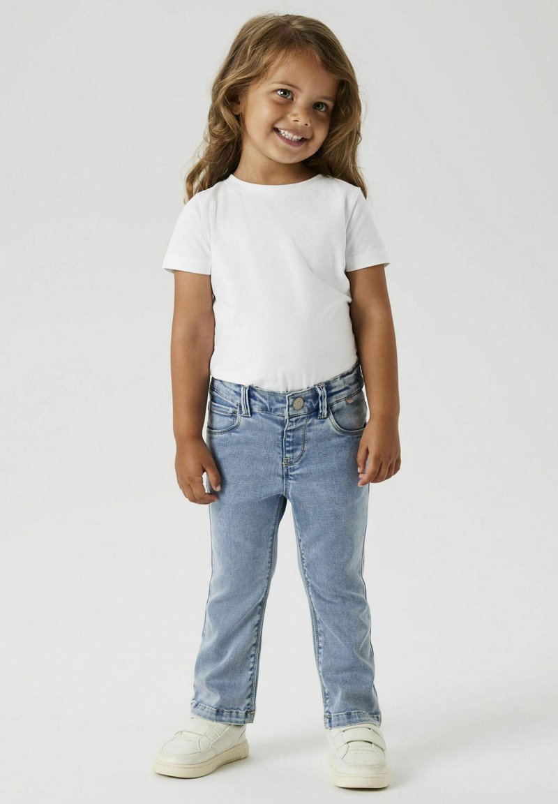 T-shirt blanc à manches courtes associé à un jean en denim bleu clair et des baskets blanches. Le jean a une coupe classique avec des poches avant.