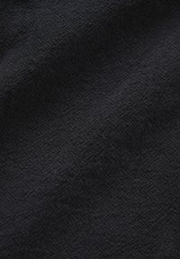 Material negru cu un model subtil texturat format din forme geometrice mici, ridicate, și pliuri moi care creează umbre luminoase.