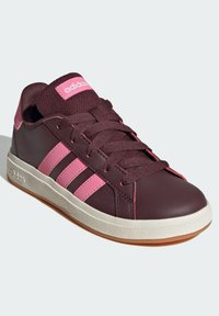 Zapatillas deportivas color marrón con acentos en rosa. Presentan tres rayas rosas en el lado, una lengüeta acolchada y una suela de goma blanca.