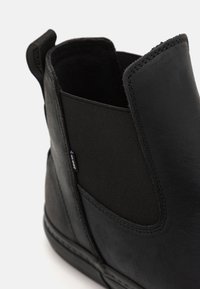 Black leather ankle boot featuring elastic side panels, rounded toe, pull tab, and reinforced stitching along the sole. Smooth texture.