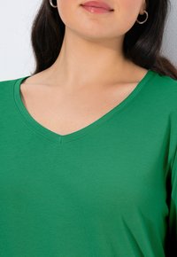 Zielony t-shirt z dekoltem w kształcie litery V wykonany z miękkiego, gładkiego materiału; charakteryzuje się prostym wzorem i luźnym krojem, z widocznym przeszyciem i bez wzorów.