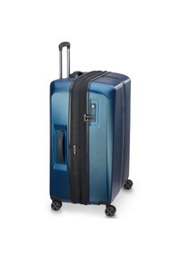 Valise rigide bleue avec fermeture éclair noire, poignée télescopique, deux roues latérales, finition texturée et détails de verrouillage par combinaison.