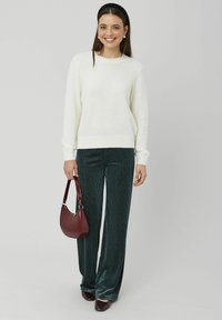 Pull crème clair avec poignets côtelés, associé à un pantalon large côtelé vert. Accessoires comprenant un sac bordeaux et des chaussures foncées.