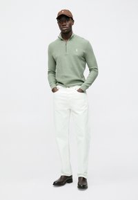 Hellgrüner Zip-up-Pullover, weiße Jeans aus Denim, braune Mütze und schwarze Stiefel. Einfaches Design mit subtiler Textur und figurbetonter Silhouette.