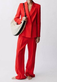 Veste en lin rouge et pantalon à jambes larges, associés à un sac souple crème et noir. Texture lisse, coupe ajustée, design moderne.