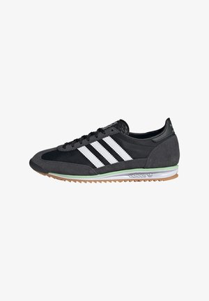 Baskets Adidas noires et grises avec trois bandes blanches, semelle en caoutchouc et accent vert sur la semelle intermédiaire, vues de profil sur fond blanc.