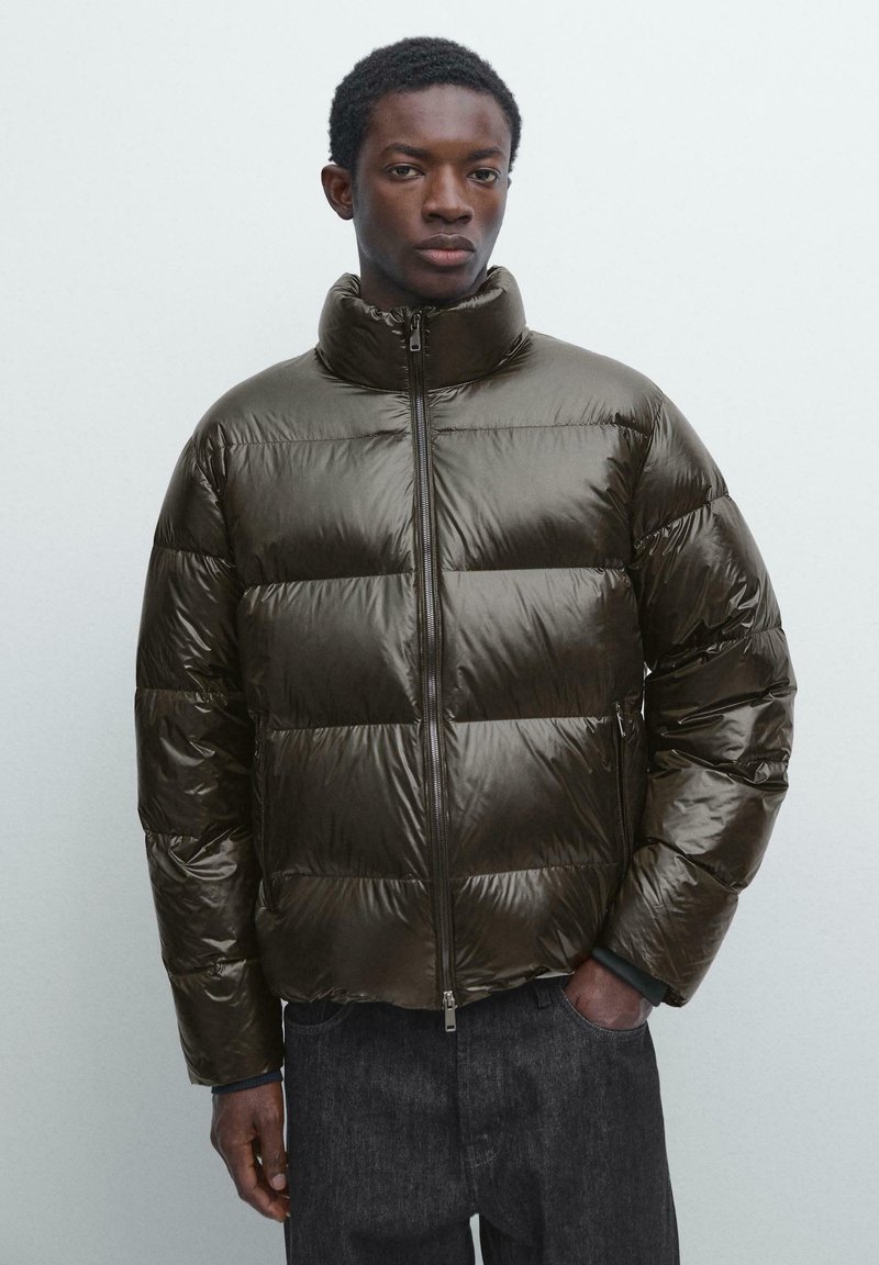 Steppjacke in Dunkelgrün mit hohem Kragen, Reißverschluss und horizontalem Steppmuster zur Isolierung. Glattes, glänzendes Material.