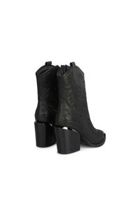 Botas de tobillo de cuero negro con patrones florales cosidos, tacones gruesos y cierre de cremallera en la parte posterior. Diseño de punta descubierta.