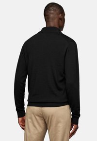 Black sweater with a textured fabric and ribbed collar and cuffs, featuring a relaxed fit and back hem ending at the waistline.