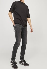 Camiseta de algodón negra con mangas cortas, combinada con jeans ajustados grises. Zapatillas negras con acentos blancos. Fondo blanco liso.