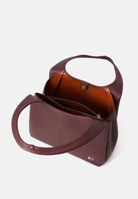 Burgundy leather tote bag with a soft texture, oval handles, open top, and an interior zip pocket featuring a brown lining. Gold hardware accent.