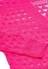 Ljusrosa stickad kofta med ett texturerat mönster och öppna detaljer. Ribbad muddar och fåll förstärker plaggets design.