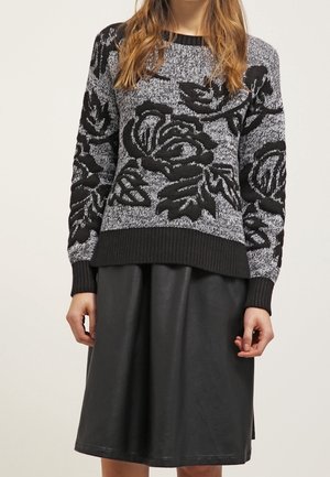 Pull en tricot noir et gris à motifs de roses, avec des manches longues, des poignets et un col côtelés, associé à une jupe en cuir noire en forme de A.