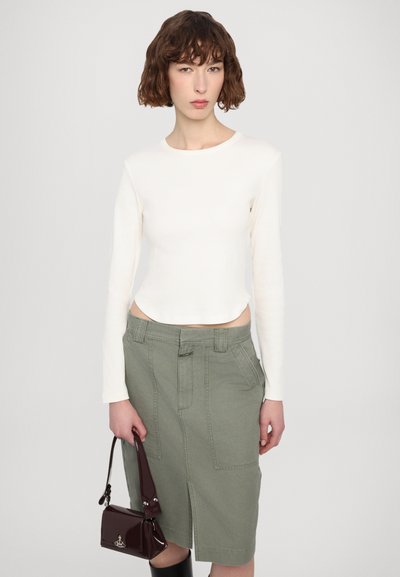 White ribbed long-sleeve top, high waist olive-green skirt with front pockets, and small dark burgundy handbag. Smooth textures and fitted design.