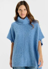 Poncho azzurro lavorato a maglia con colletto alto e spesso, maniche corte e tessuto strutturato. Presenta una vestibilità rilassata e spacchi laterali per il movimento.