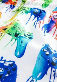 Färgglada badshorts med ett mönster av droppande videogame-kontroller i grönt, blått och orange på en vit bakgrund.