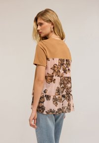 Hnědý top s krátkým rukávem s květinovým vzorem na světle růžové panelu na zadní straně. Lehce materiál s uvolněným střihem. Neformální styl.