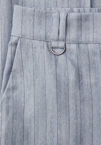 Pantalon gris clair à fines rayures verticales foncées, avec une boucle de ceinture et un petit détail en forme de D en argent.