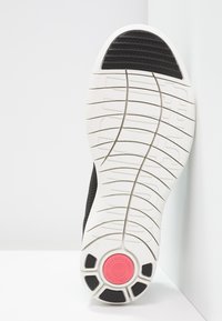 Zwart atletisch schoenzool met een witte rubberen tussenzool, een gestructureerd grippatroon en een roze accent op de hiel.