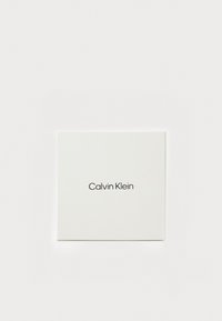 Weißer quadratischer Kasten mit "Calvin Klein" in schwarzem Text auf der Vorderseite, mit einer glatten, matten Oberfläche.