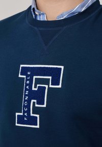 Felpa blu navy con un logo "F" ricamato in bianco e blu, testurizzato. Presenta un colletto a costine e dettagli a punto festone sullo scollo.