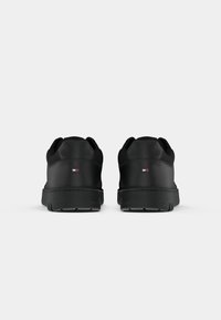 Paire de baskets basses noires vues de dos avec un petit logo rectangulaire présentant des rayures rouges, blanches et bleues sur chaque talon.