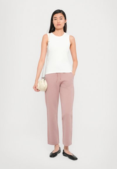 White sleeveless top, soft pink trousers, black flats, and a cream handbag with chain. Fitted and tailored design with straight leg shape.