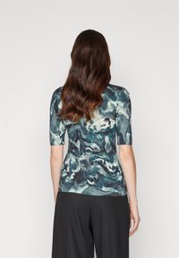 Kortärmad stickad topp med ett abstrakt mönster i blått och grönt, med en slät yta och figurnära design, sedd bakifrån.