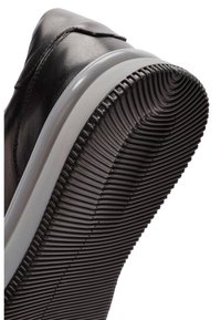 Zapatilla de cuero negro con una suela de goma gris flexible que presenta un patrón texturizado y acanalado para ofrecer agarre y durabilidad.