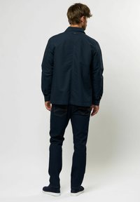 Chaqueta azul marino con cuello abotonado, hecha de un tejido suave. Combinada con jeans de mezclilla oscuros que tienen costuras en contraste.